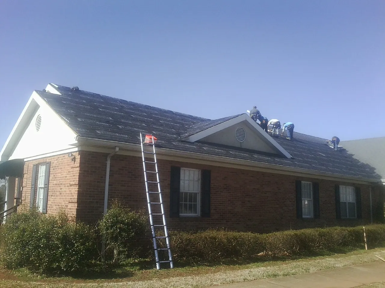 Crew tearing shingles off a brick ranch roof with a ladder set — Emergency Roof Repair work by our crew in Medaryville