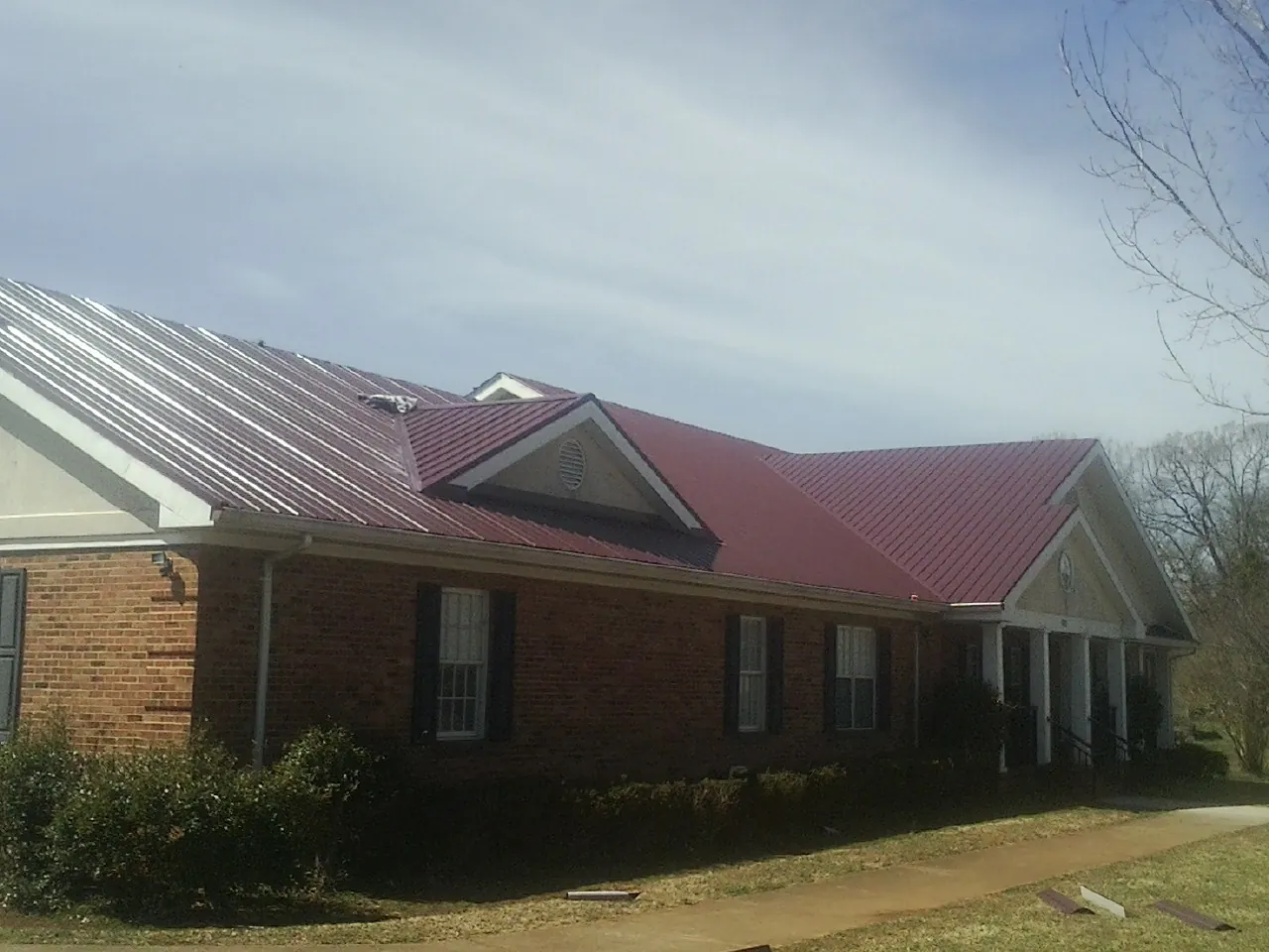 Red metal roof with gabled entries on a long brick building, from a Hail Damage Roof Repair job in Medaryville