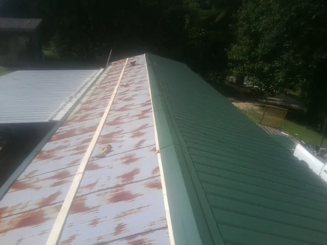 Old rusted panels beside newly installed green metal roofing — Wind Damage Roof Repair by Roofing Brothers in Medaryville