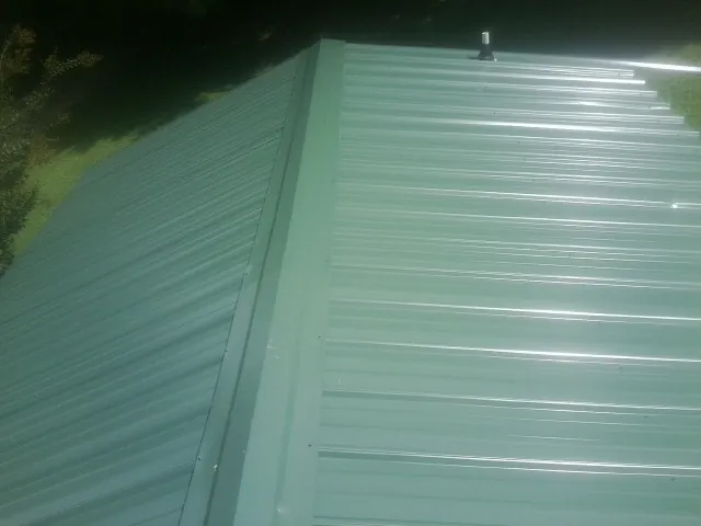 New green metal panels meeting at the ridge of a roof — Flat Roof Repair work by our crew in Medaryville