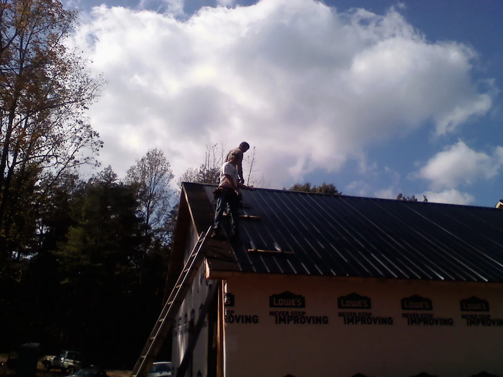 Roofer fastening dark metal panels high against a cloudy sky, from a Roof Inspection job in Medaryville