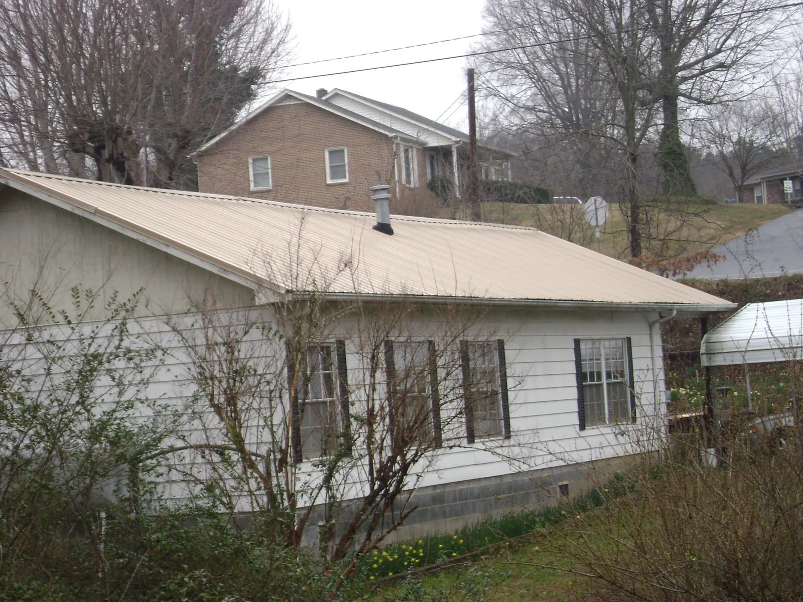 Tan metal roof on a white sided house set into a hillside — Commercial Roofing by Roofing Brothers in Medaryville
